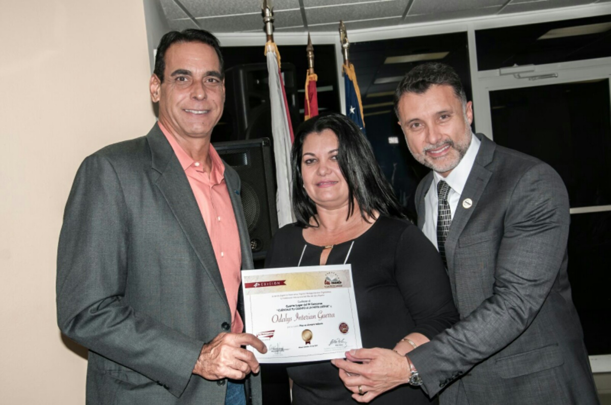 La escritora Odalys Interian Guerra, ganadora del cuarto lugar, recibe el reconocimiento de parte de Albert Collazo, gerente de comunicaciones de Ford y Luis Castillo, gerente de comercialización de PAWA.